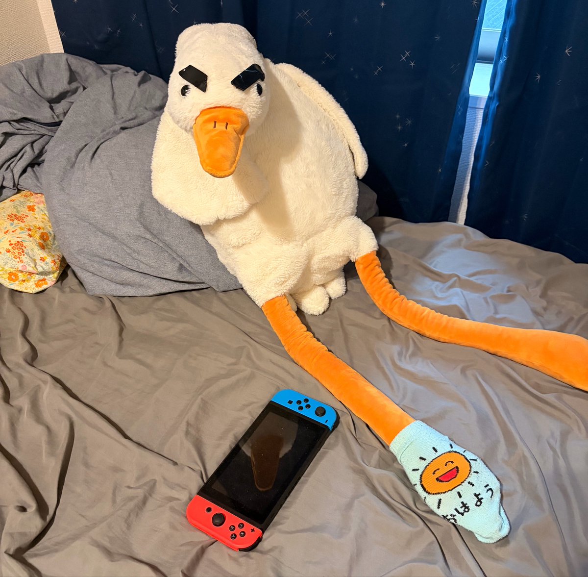 A giant white duck plush with thick black eyebrows lounging on a bed
